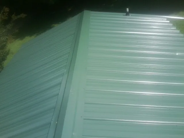 New green metal panels meeting at the ridge of a roof — Flat Roof Repair work by our crew in Revere
