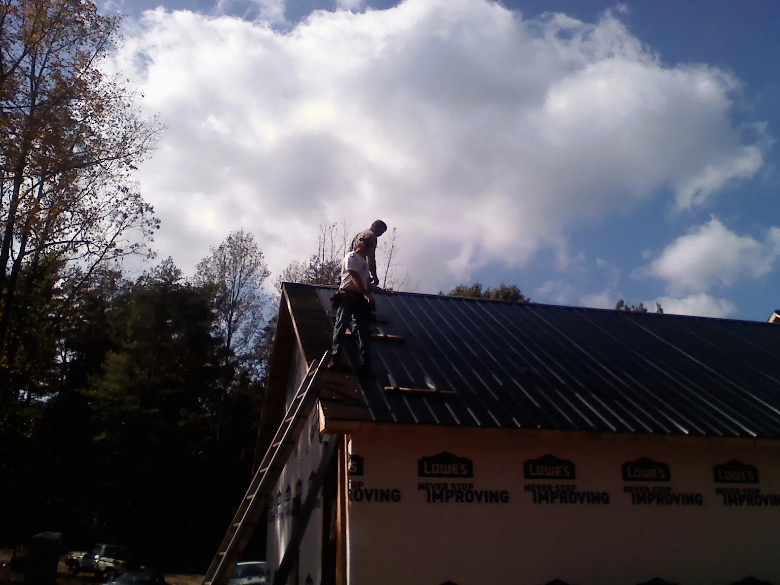 Roofer fastening dark metal panels high against a cloudy sky, from a Roof Inspection job in Revere