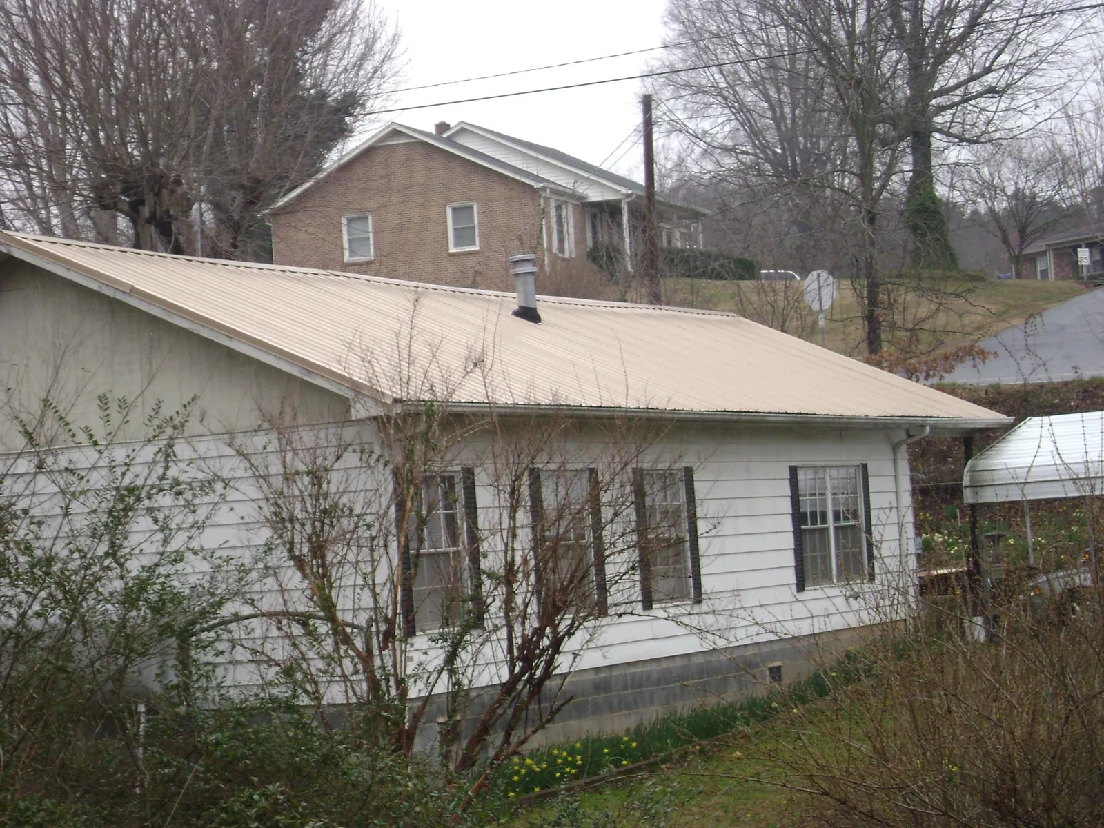 Tan metal roof on a white sided house set into a hillside — Commercial Roofing by Roofing Brothers in Revere